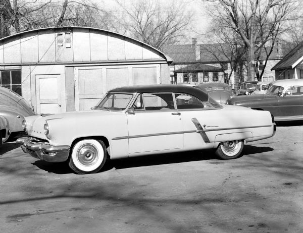 An automobile parked in front of a Trachte building at King's Korner used car lot, 1102 East Washington Avenue. King's Korner is owned by King Motors Incorporated, the largest Lincoln-Mercury dealer in Wisconsin, located at 1501 Monroe Street.
