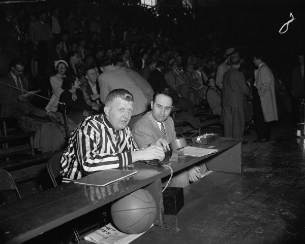 Jim Gunderson, official scorer at the state high school basketball tournament, wears a striped referee shirt while sitting alongside LaVerne Van Dyke, assistant basketball coach at the University of Wisconsin, at a tournament. This is the first year that the official scorer at the basketball tournament started wearing a black and white striped shirt so that substitution players entering the games can now easily report to the correct official along the officials' table.