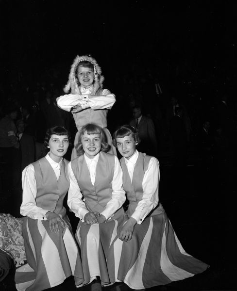 Group portrait of the Tomah High School "Indians" cheerleaders at the state high school basketball tournament. Seated, left to right, are Connie Schmalz, Mary Klinge, and Deanna Detlie. Standing and wearing a headdress is Sandra Zallmer.