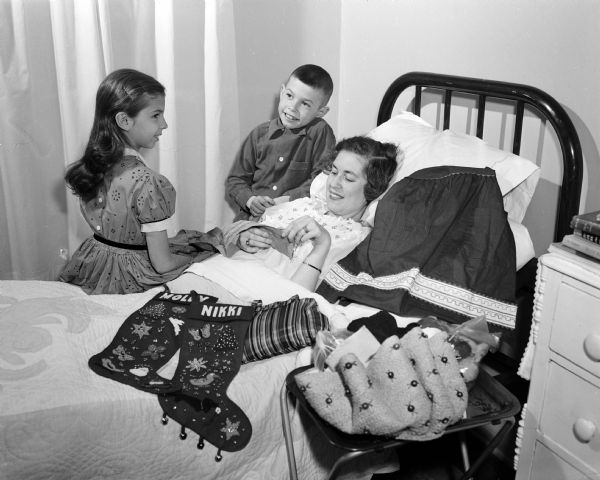 Elsie Smavy (right), bedridden in her seventh year of polio and with limited movement in her lower arms, creates embroidery. Her children, Molly, 7, and Nikki, 8, look on.