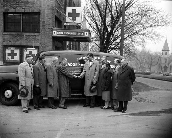 Group portrait in front of the Badger Regional Blood Center, 302 East Washington Avenue. Dr. Merle O. Hamel acted as director. The people stand around a new American Red Cross van presented on behalf of the Fraternal Insurance Societies by the National Fraternal Congress of America.