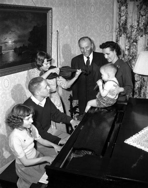 The musical Dvorak family posed around a piano. Left to right, they are: Theresa, 11, Robert,15, Katharine,12, holding a violin, the father Professor Raymond Dvorak, Tony, 2, seated atop the piano, and the mother, Florence. Professor Dvorak was a University of Wisconsin professor of music and director of university bands.