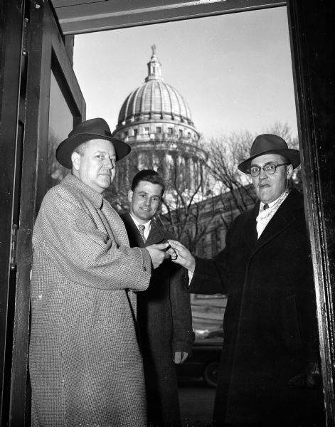 City Inspection Superintendent Ray Burt handing the key to City Hall to Merrill Hays, who represents an investment group that purchased the building. William Haley is shown in back, with the Wisconsin State Capitol building in the background.