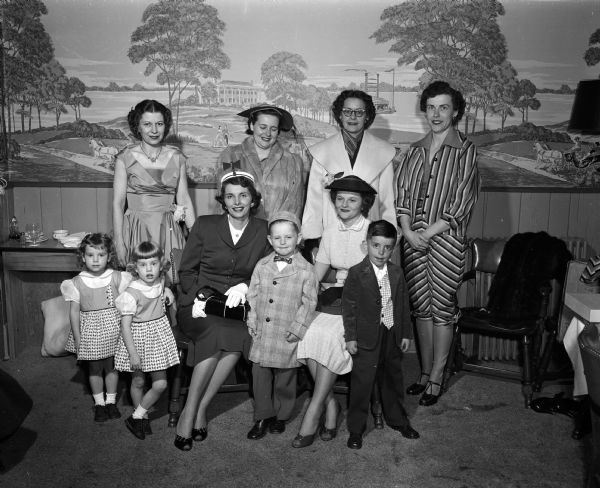 Group portrait of models for the Exchange Club style show, including women and children. Back row left to right: Ruth Arnold, Mrs. Douglas Schmale, Mary Thomas, Kathryn Jones. Front row left to right: the Graham twins, Audrey Presenza, Larry Schmale, Muriel Taubert, and Steve Presenza.