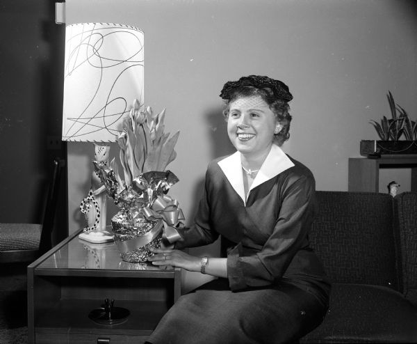 Mrs. John V. Mc Keon posing beside a floral arrangement while wearing an Easter hat.