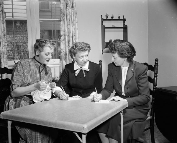 The Dane County Republican Women's Club plans bridge parties to raise funds. Seated at a table, left to right are: Christine Beggs, Helen Karberg, and Frances Nestingen.