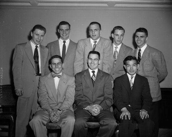Portrait of eight key members of the University of Wisconsin boxing team at the annual banquet. Front row, left to right, are: Charlie Magestro, a co-captain for the 1955 team; Robert Morgan, a 1952 NCAA champion; and Roy Kuboyama, a 1952 NCAA champion. Back row, left to right, are: Terry Tynan, a co-captain for the 1955 team; Bobby Meath, a 1954 NCAA champion and winner of the George Downer Trophy; Ray Zale, a 1953 NCAA champion; Jim Schneider, the outstanding freshman boxer; and Bobby Goodsitt, winner of the Jack Ferguson trophy for the "Unknown Champ." Tynan and Magestro were also named co-winners of the "Chin Up and Hands Down Club."