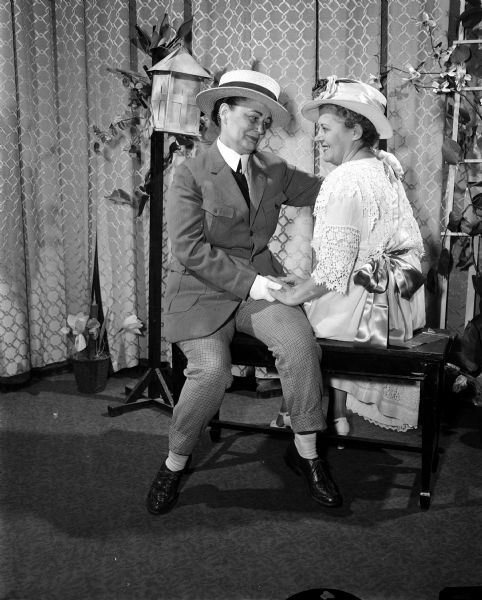 One of a series of scenes from the dramatic production "Down Memory Lane", presented in celebration of the 60th anniversary of the founding of the Madison Woman's Club. During the skit "Strolling Though the Park One Day", a couple are seated on a bench. At left, Elizabeth Coulter plays a "swain" and Sylvia Hoppe sits beside her.