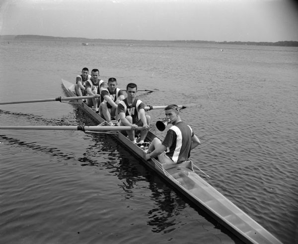 Four rowers and a coxswain posing in their boat. All five students were named Smith. Left to right, their first names are Jim, Irv, Dick, Foster, and Stan.