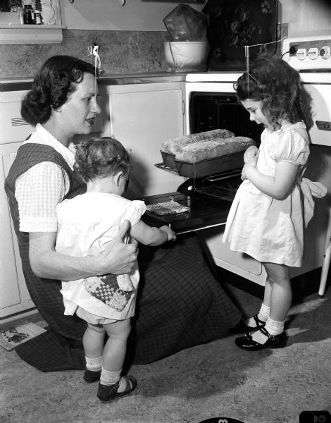 Elizabeth Morris takes loaves of bread out of the oven as her children Mary, age 3 1/2 and Sandra, 15 months, look on. The photograph was taken as part of a Mother's Day article featuring the many roles performed by stay-at-home mothers.