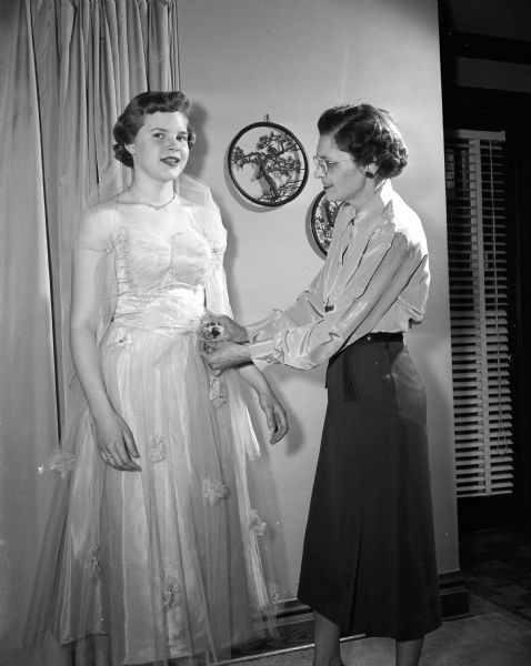Frances Larson putting the final touches on a formal dress modeled by her daughter Laurie, age 14. Frances, labeled a "modiste" or one who makes fashionable dresses, made the dress for her daughter.