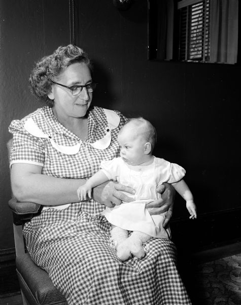Mrs. Jack Schwartz of Roxbury holding a 3-month-old baby girl on her lap. The child is one of the nearly 60 foster children that Mrs. Schwartz has cared for in the last seven years. She and Mr. Schwartz also raised seven children of their own.
