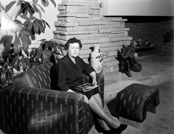 Mrs. C.S. Gonstead sits next to the fireplace in her home (aka "El Clare" estate) at 602 South 2nd Street in Mt. Horeb. Madison architect Herbert Fritz designed the house, which was built in 1951 and severely damaged by fire in 1991. The accompanying newspaper article describes some of the architectural highlights and the decorative features added by the Gonsteads, especially their Chinese and Japanese furnishings and ornaments.