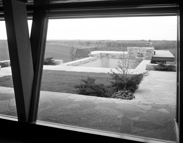 View through the living room's south wall window of the flagstone terrace, swimming pool, and bathhouse of the S.C. Gonstead residence in Mt. Horeb. Madison architect Herb Fritz designed the house, which was built in 1951 and severely damaged by fire in 1991. The accompanying newspaper article describes some of the architectural highlights and the decorative features added by the Gonsteads, especially their Chinese and Japanese furnishings and ornaments.