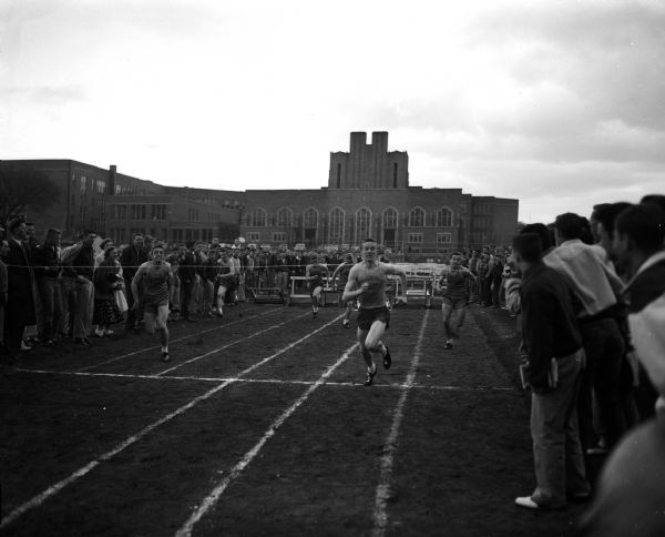 Participants cross the finish line of the high hurdle race at the city track meet, held at the Madison East High School athletic field. Dean Hewitt of East was the winner, with his teammate John Cnare coming in second. At right is Dave Johnson of West who was third.