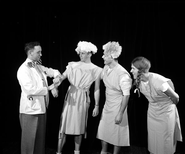 Actors participate in a University of Wisconsin Medical School junior class skit during Field Day for the medical students. This skit is about physical examinations given to entering freshmen. Eugene Weston, left, portrays the examining physician. Freshmen students, dressed like characters from a Haresfoot show are, left to right: Harry Groth, Thomas O. Miller, and Richard Holder. 

Field Day is an annual event in which research papers are presented, and various departments have exhibits on their research work, culminating in a banquet and skits by members of the junior class.