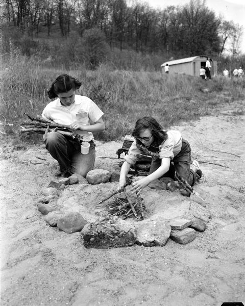Joan Mani and Annetta Evert arrange a spot for cooking over a fire in the sand during the annual seventh and eighth grade play day of the Black Hawk Council of the Girl Scouts at Camp Brandenburg.