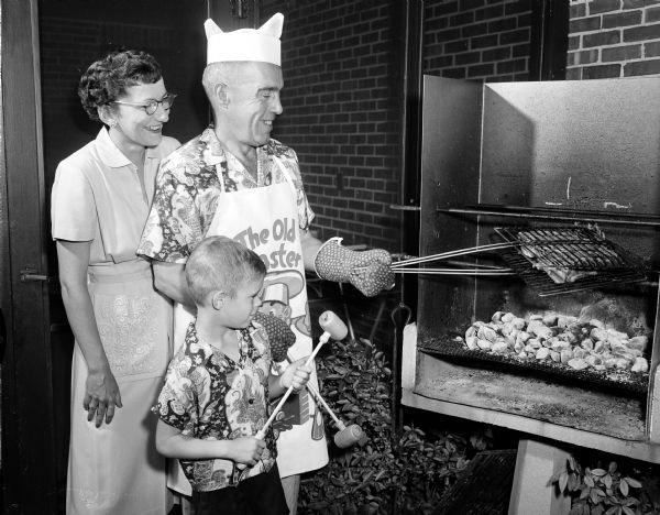 Doctor Lawrence V. Littig cooking a steak on a grill while his wife Sally and seven-year-old son Norman look on.