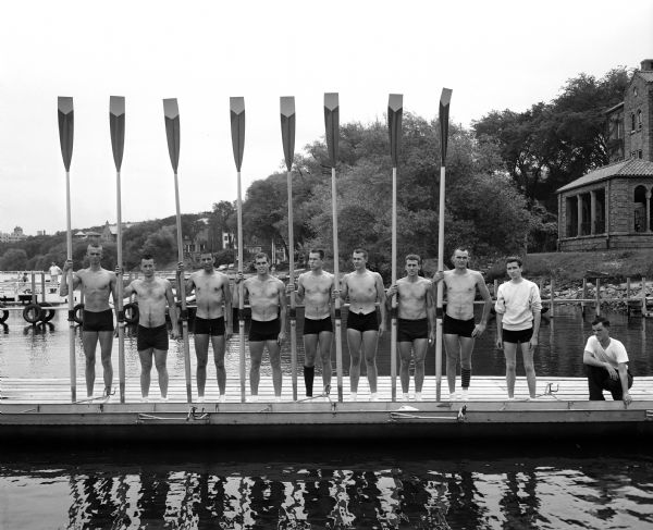 Members of the University of California male varsity crew stand on a pier at the shore of Lake Mendota.
