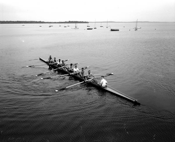 Members of the University of Wisconsin male crew row on Lake Mendota. Picnic Point is in the background.