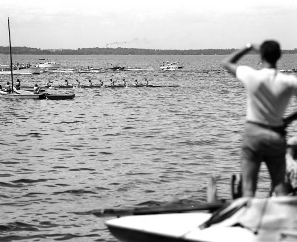 A man in the foreground is looking out over Lake Mendota as the University of Wisconsin varsity crew beats the California Golden Bears by 10 feet in a late spurt to win in record time.