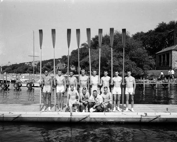 Members of the male University of Wisconsin varsity crew stand on the dock while holding oars.