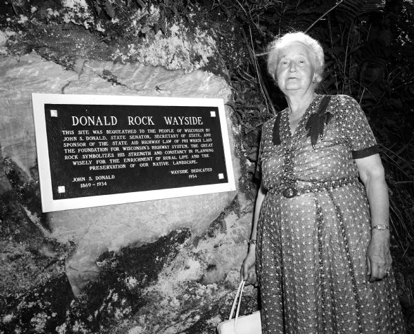 Vona Donald poses next to a newly dedicated plague. The occasion was the opening of a new wayside park located along Highway 92 between Mt. Horeb and Mt. Vernon. It was named Donald Rock Wayside Park in honor of her late husband, John S. Donald. The plaque reads: "The site was bequeathed by Mr. Donald, who died in 1934. He served the state as senator and secretary of state, and was a sponsor of the State Highway Aid law of 1911, which formed the framework for the state's highway system."