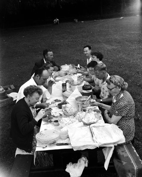 Three families picnic in Vilas Park. Clockwise around the table are: Mr. & Mrs. Thomas Brewer, New Lisbon, Benny & Doris Hendrickson, 113 West Broadway, Madison and Mr. & Mrs. Lester Hall, New Lisbon, Tommy Brewer Jr., Lowell Hendrickson and Elizabeth Rust, New Lisbon.
