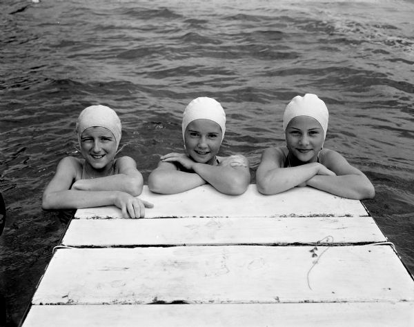 Three teenage swimmers lean on the edge of the pier at Camp Maria Olbrich, a YWCA Teen Camp on the shore of Lake Mendota. The girls are, left to right: Bonnie Jinkins, daughter of Mr. and Mrs. Clinton Jinkins, 1014 W. Dayton St.; Bette Jestila, daughter of Mr. and Mrs. Fred Jestila, 2817 Van Hise Avenue and Bonnie Sorenson, daughter of Mr. and Mrs. H.S. Sorenson, 2129 Oakridge Avenue.