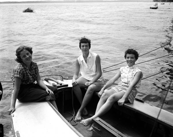 Three sailing enthusiasts at Camp Maria Olbrich, a YWCA Teen Camp on the shore of Lake Mendota, sit in a sailboat. Sheila Owens, left, granddaughter of Mrs. Frank J. Owens, 735 Williamson Street and Barbara Berger, right, daughter of Dr. and Mrs. John V. Berger, Jr., 902 Cornell Court are being instructed by Mrs. William Reynolds, Evansville, who is in charge of sailing and horseback riding at the camp.