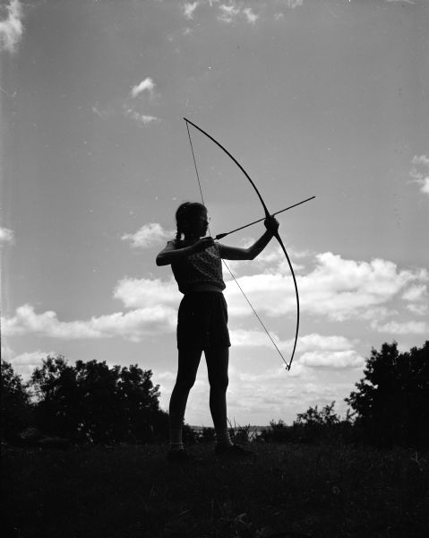 Evelyn Howe, daughter of Professor and Mrs. Herbert Marshall Howe, 2022 Chadbourne Avenue, practices archery at Camp Maria Olbrich, a YWCA Teen Camp located on the shore of Lake Mendota.