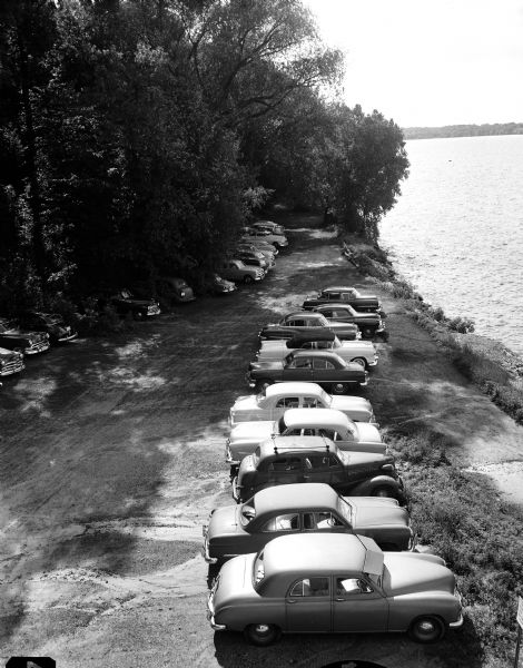 Elevated view of the University of Wisconsin Hydraulics Laboratory at 660 North Park Street. Automobiles are parked along Lake Mendota shoreline in front of the laboratory, with Picnic Point in the background.