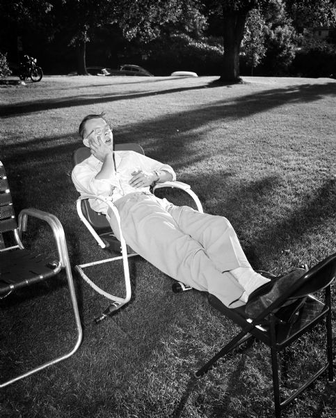 A man reclines in a chair outdoors with his feet resting on another chair.