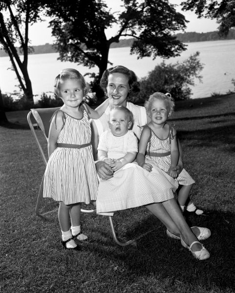 Outdoor group portrait of Suzanne Schmidt with her three children. Left to right: Deborah, Erwin III, and Susan. They are seated in the backyard at the home of her parents, Mr. and Mrs. Richard Boissard of Maple Bluff.