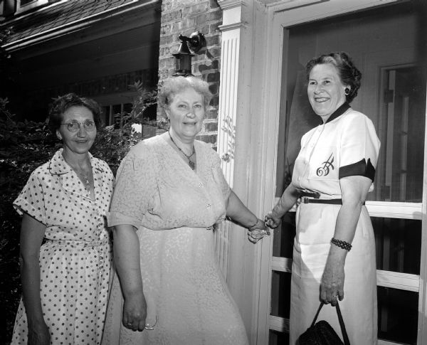 Group portrait of Florence Koehler, president of the church women's association, Leora Phillips, and Miriam Stroud. They are posing by the front door at 739 Farwell Drive in Maple Bluff.
