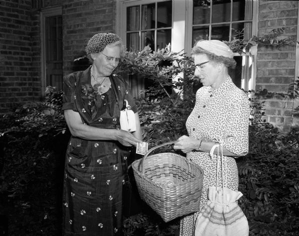 Esther Hauver puts money into a basket held by Nettie Stafford. Proceeds from the Missionary tea will go to the Embudo Presbyterian Hospital in New Mexico and the Christian Medical Training College in Tudhiana, India. The tea was held at 739 Farwell Drive in Maple Bluff.