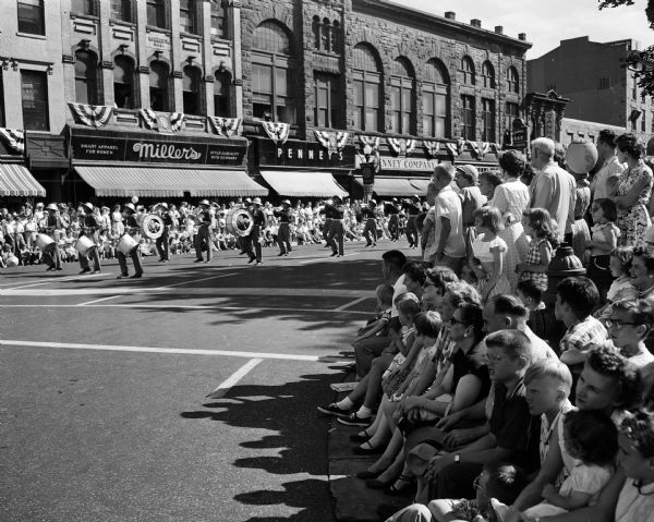 The crowd watches a marching unit along East Main Street during the American Legion parade around the Capitol Square. Miller's and Penny's are in the background.