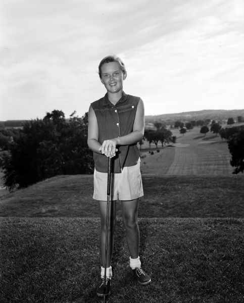 Twelve year old Carol Sorenson of Janesville stands on a golf course with a golf club. She will compete with Marilyn Hall of Milwaukee for the junior golf championship of the Wisconsin Women's Golf Association to be held at the Blackhawk Country Club.
