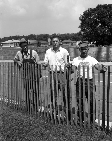 Outdoor group portrait of city streets department personnel Vincent Mongold (left), Gene Westbury, and Tony Cardarello Jr. The men helped set up the race track, and are standing behind snow fences that will keep spectators away from the soap box derby racing lanes on South Midvale Boulevard.