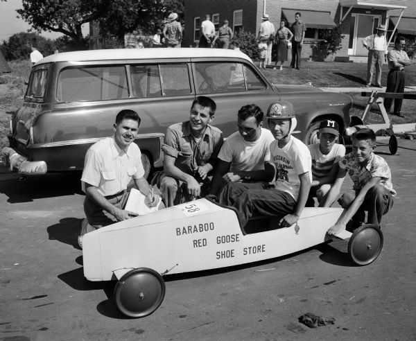 Three former Madison soap box derby champions give pointers to one of the 1954 entrants, Terry Frambs of Baraboo. Behind the racer, left to right, are 1947 champion Dick Brilliott, 1950 champion Warren Slightam, and 1951 champion Rod Botts.