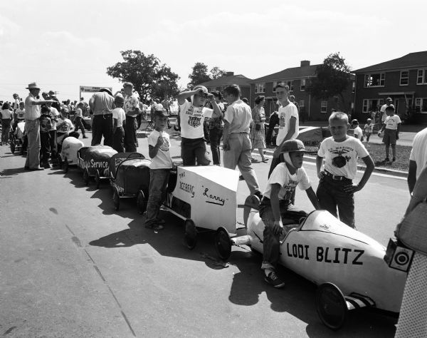 A lineup of racers await their turn to race at the 1954 Madison soap box derby. Larry Meicher of Madison stands by his racer, "The Iceberg." The are at the top of Midvale Boulevard.