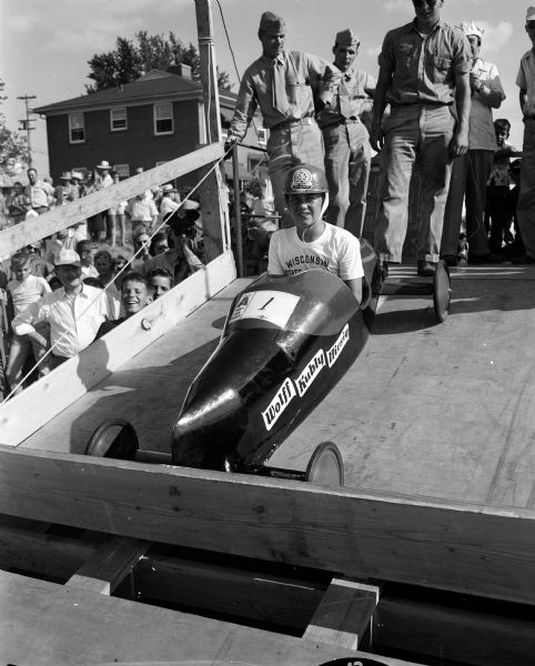 Phil Peckham of Madison is ready to start his winning heat during the 1954 Madison soap box derby. Members of the Marine Corps Reserve are shown operating the starting board. The starting line is at the top of Midvale Blvd.