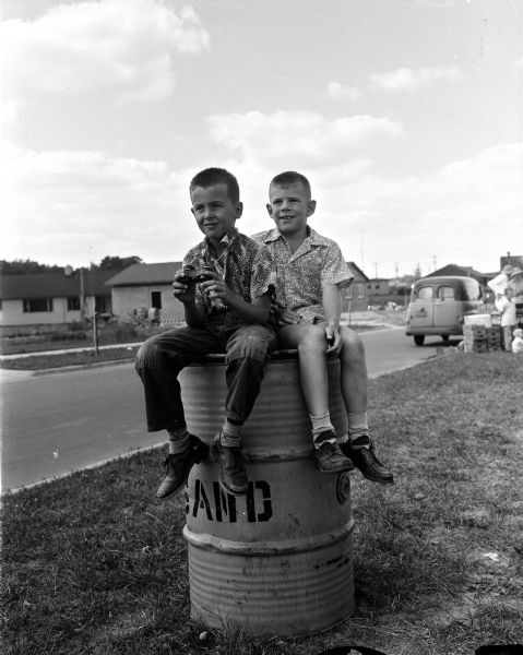 Artie Luetke and Dick Michels sitting on top of a sand barrel to watch the 1954 Madison soap box derby races.