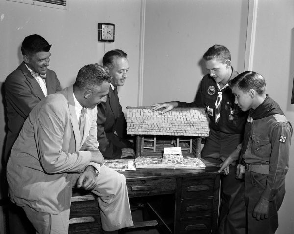 Two United Givers campaign fund officials inspect a Boy Scout project, a model log home. Left to right: William E. Corder, Scout executive; F. Leon Sanna, chairman of the Area Business division of the fund; Irwin J. Lackore, Sanna's associate in the October drive; Explorer Scout Dick Liefer and Boy Scout Jerry Martinson.