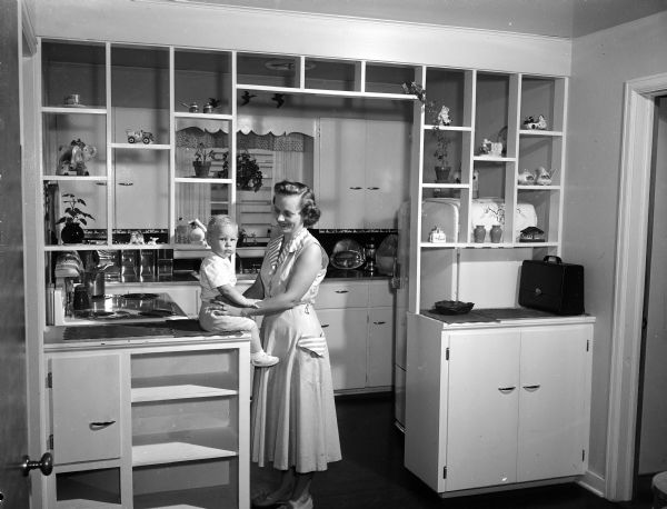 Evelyn Kurth and 14-month old Terry Kurth pose in the kitchen of Harold and Evelyn's home at 2 Harding Street in Madison. The room features a trellis-like partition Harold Kurth devised to divide the kitchen into dinette and kitchen space.