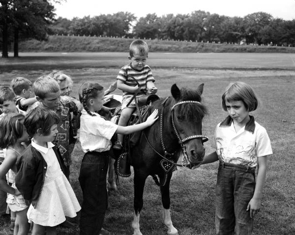 Pony rides are given to children at the Franklin School playground. Left to right: Patty Fitzgerald, Jimmie Schaub (on pony), Frances Orvold. Several other unidentified children cluster in back of Frances Orvold, but not in the published newspaper photograph.