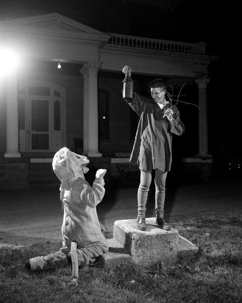 A scene from the Mineral Point Players' production of Shakespeare's "A Midsummer Night's Dream." James Dolan enacts the role of Moonlight by standing on an old carriage step and raising a lantern. In front of him is Ernie Springer as the lion. In the background is the Gundry Mansion, owned by the Mineral Point Historical Society.