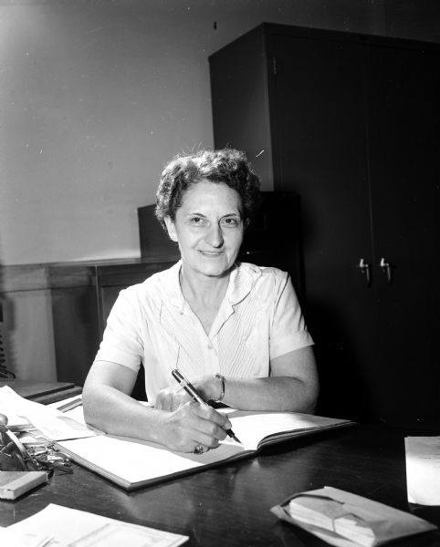 Portrait of Ruth Schnurbusch, seated at a desk. She is an office secretary for the Building and Construction Trades Council, and secretary for the Electrical Workers' Local 159.