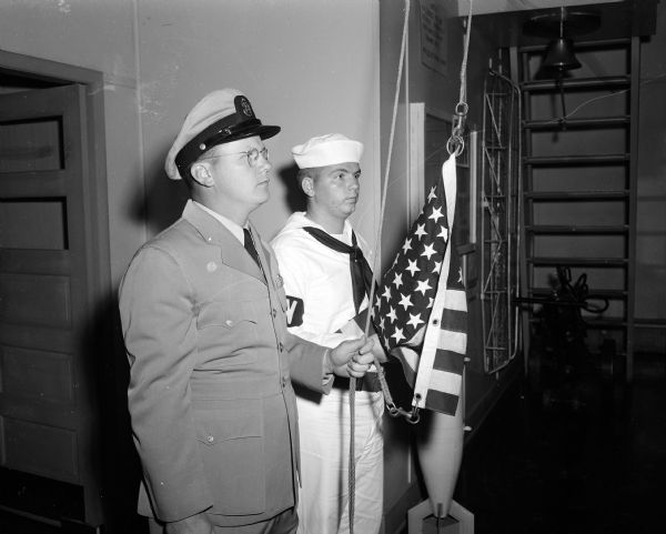 Chief Boilertender Marvin Severson (left) and Seaman Apprentice Malcolm Astin raise the colors at the Madison Naval Reserve Surface Division at the Naval Reserve Training Center at 1046 East Washington Avenue.