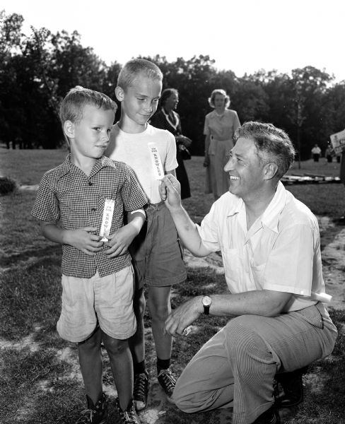 State Senator Warren Knowles, (R-New Richmond), Republican-endorsed candidate for lieutenant governor (right), crouches to greet Tom and Bill Jasper, two young brothers wearing campaign ribbons on their shirts. The picnic was at Westmoreland Park.